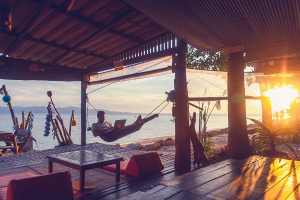 Man laying in hammock and working on laptop during sunset